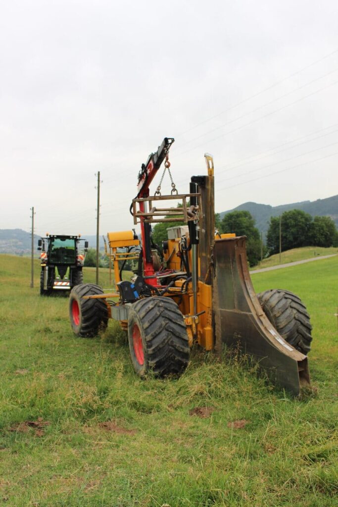 Auf einen Feld steht eine Einpflügmaschine zum verlegen von Kabel, Leitungen und Rohren. Im Hintergrund steht ein Traktor.