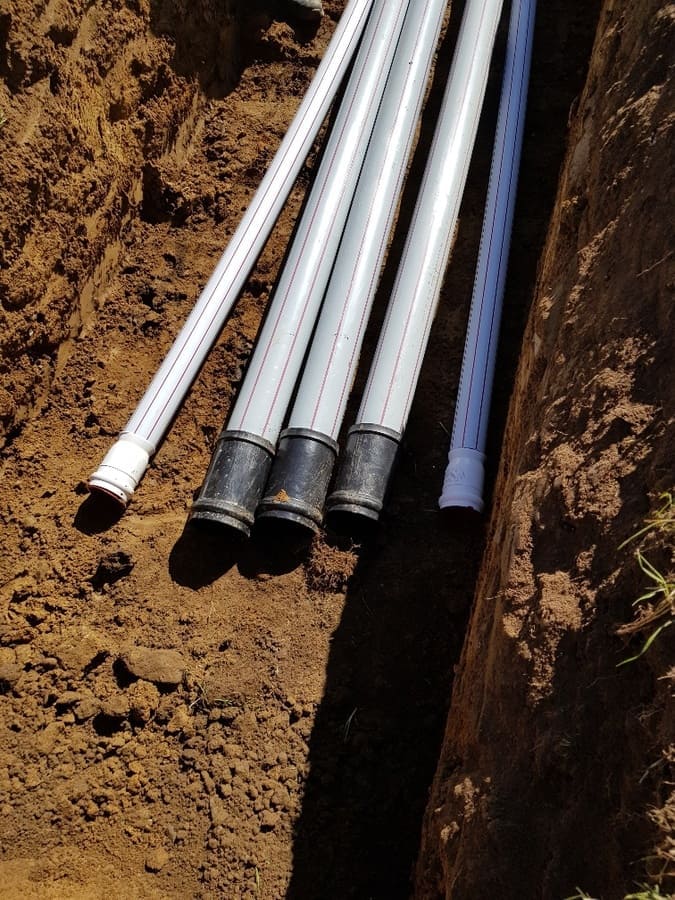 Fünf weisse Rohre liegen bereit im Graben, für den Leitungsbau, zur Montage bestimmt. Sie sind bereit, in die Erde gelegt zu werden, um wichtige Verbindungen herzustellen und den Transport von Flüssigkeiten zu ermöglichen.