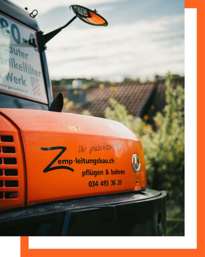 Auf dem hinteren Teil eines Baggers prangt das Logo der renommierten Firma Zemp Leitungs- und Tiefbau GmbH. Dieses Logo symbolisiert Qualität, Fachkompetenz und Innovation, Werte, die das Unternehmen seit Jahren erfolgreich verkörpert